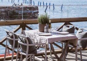 Una terraza de madera con una mesa preparada para dos, con vista a un cuerpo de agua.