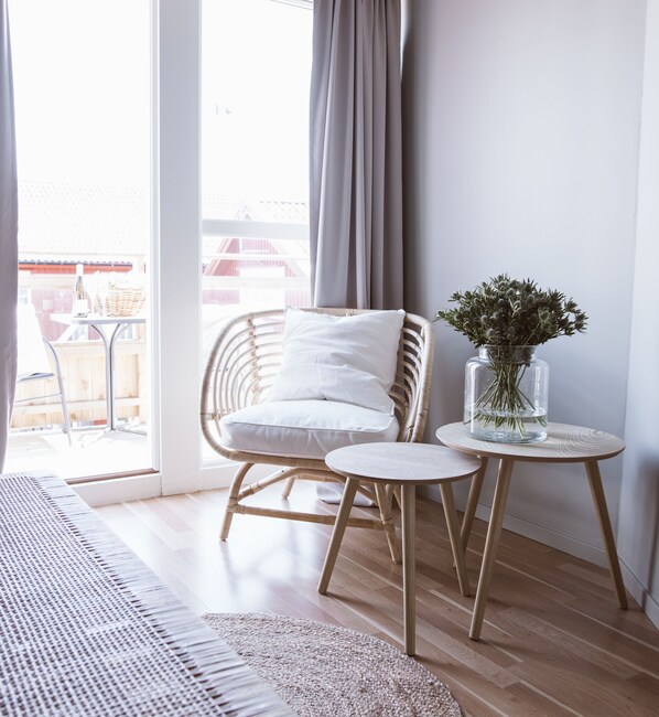 A room with a wicker chair, a small round table, and a vase with greenery.