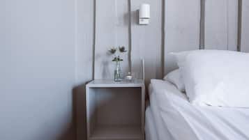 A minimalist bedroom with a white bed, a small bedside table, and a wall-mounted light.
