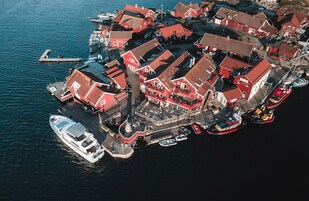 Vista aérea de un pueblo costero con edificios de techo rojo, un muelle con barcos y un pequeño embarcadero.