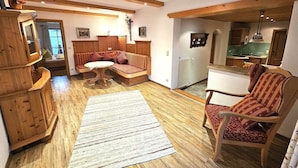 Ein gemütliches Wohnzimmer mit einer Couch, einem Holzschrank, einem Esstisch und einem durch einen Bogen sichtbaren Küchenbereich.