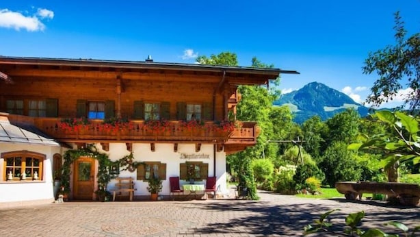 Ein traditionelles Holzhaus mit einem Balkon, einem gepflasterten Innenhof und einem Blick auf die Berge.