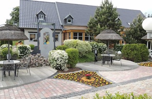 Ein Innenhof mit Außenbestuhlung, einer Steinmauer und einem Gebäude mit grauen Ziegeln auf dem Dach.