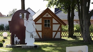 A park entrance with a white statue of a man holding a light bulb, a cat silhouette, and a sign reading "Parkplatz L". - Haffblick (1) - Landhaus Mönkebude (Mönkebude)