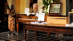 Un suelo a cuadros, una mesa de madera con un florero, un cuadro enmarco y una estatua.