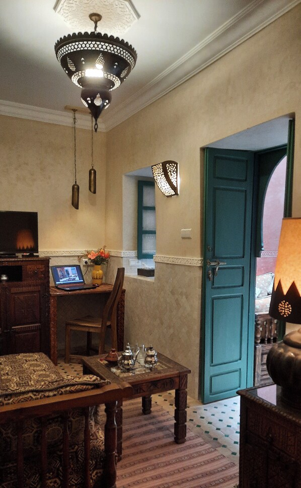 A traditional room with a wooden table, a television, a laptop, a decorative lamp, and a blue door.