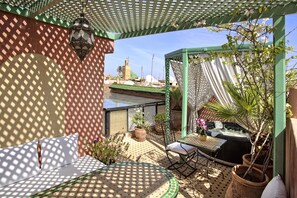 A patio with a table, chairs, and a hot tub. There are potted plants and a pergola with a white curtain.