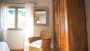 A room with a wicker chair, a wooden wardrobe, a window with curtains, and a tiled floor. - House with pool and river access (Fontaine-de-Vaucluse)