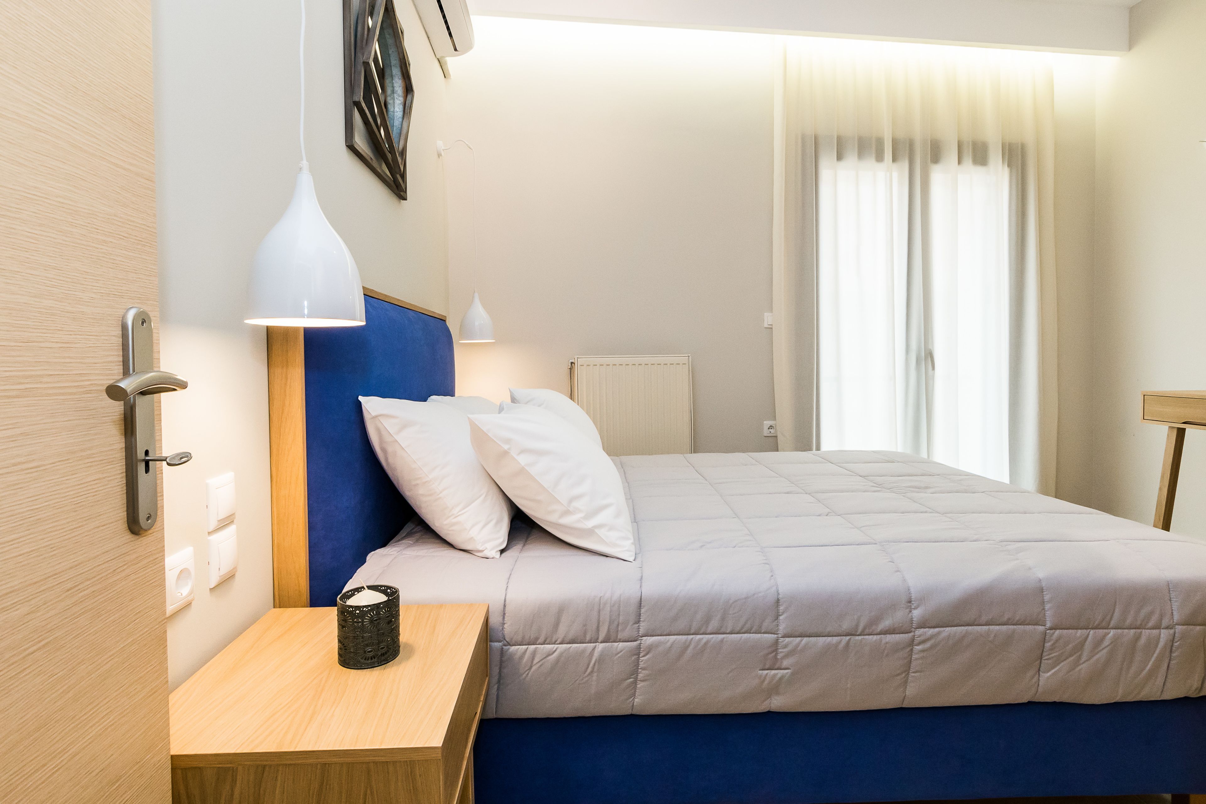 Una habitación de hotel con cama, mesita de noche, lámpara y vistas al exterior por una ventana.