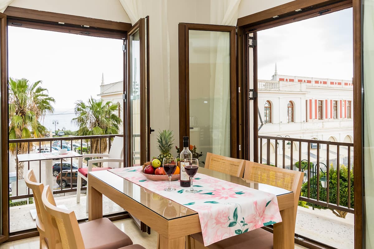A balcony with a dining table set for two, featuring a floral tablecloth, two chairs, and a fruit bowl.
