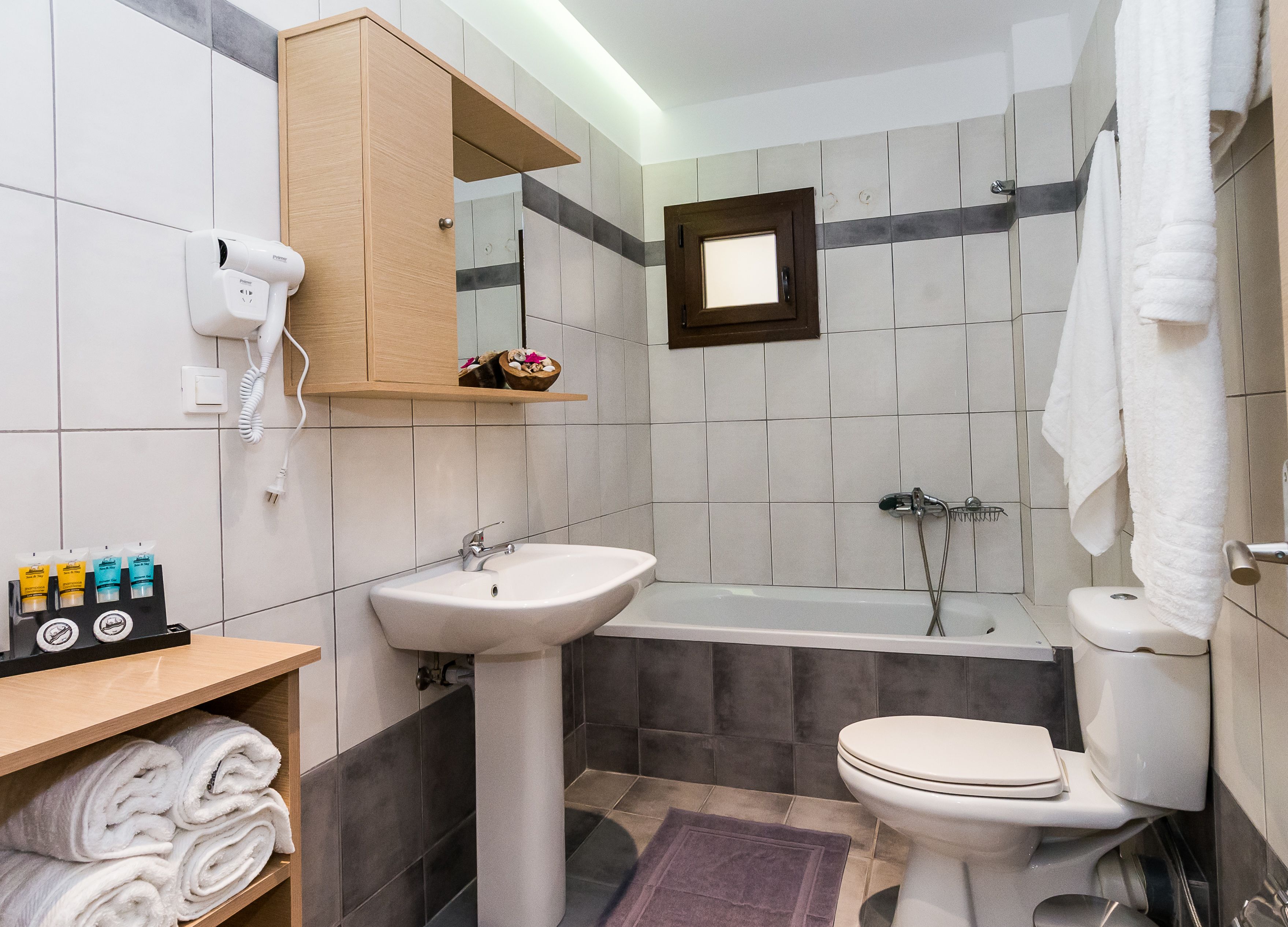Een badkamer met een wastafel, toilet en douche. Handdoeken en toiletartikelen liggen op planken.