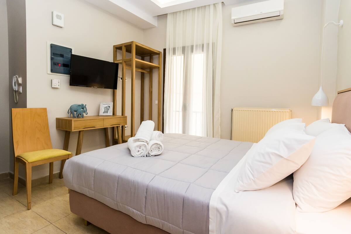 A hotel room with a bed, a desk, a chair, a TV, and a window with curtains.