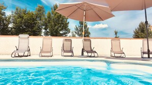 A swimming pool with six lounge chairs and two umbrellas.