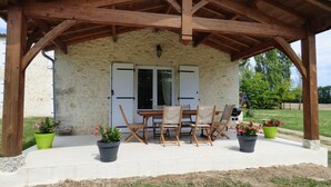 A covered outdoor seating area with a stone wall, wooden table and chairs, and potted plants.