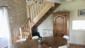 A dining area with a round table, white chairs, a wooden cabinet, and a staircase.