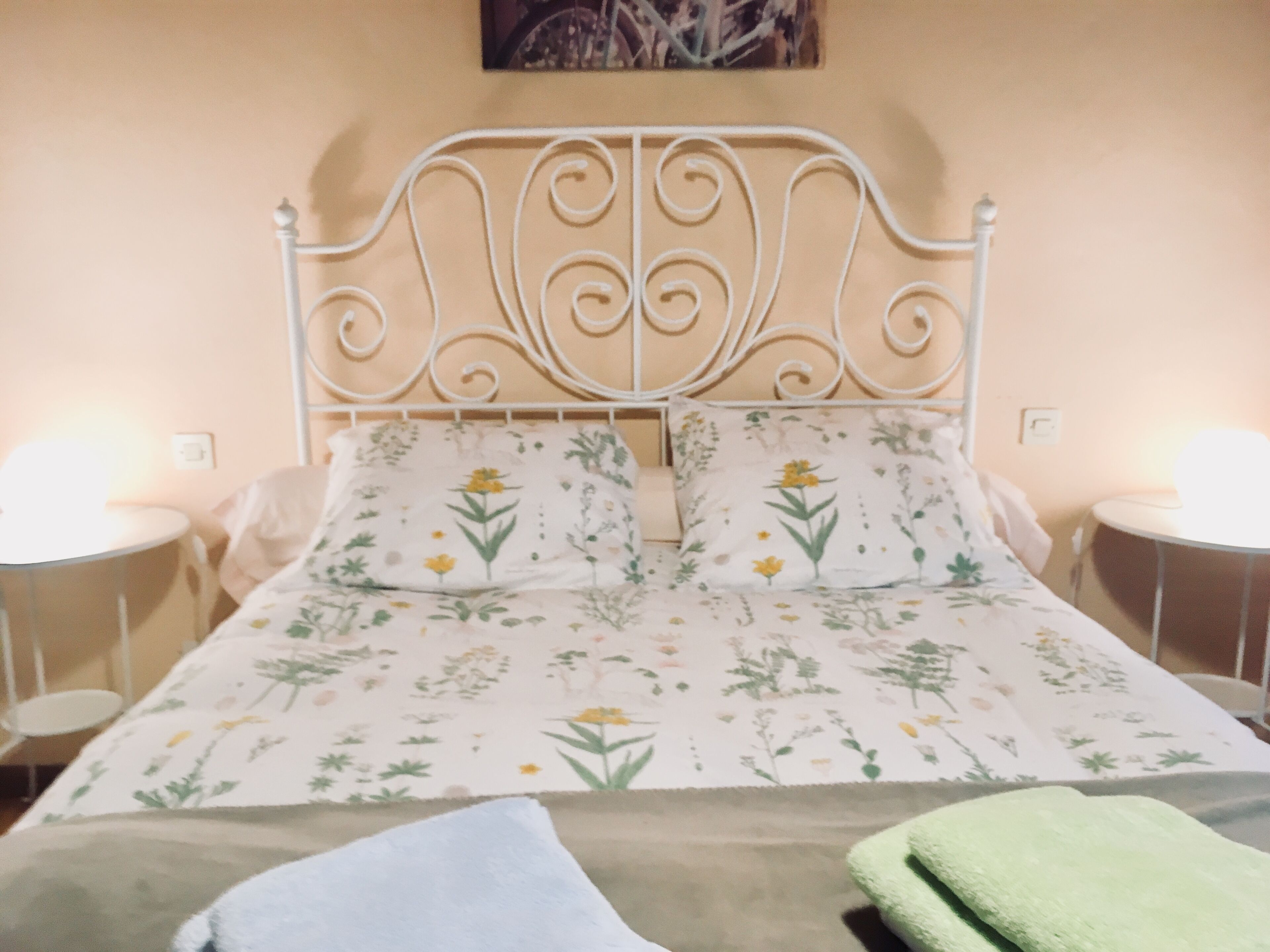 A bed with a floral bedspread, two bedside lamps, and a green towel on the bed.