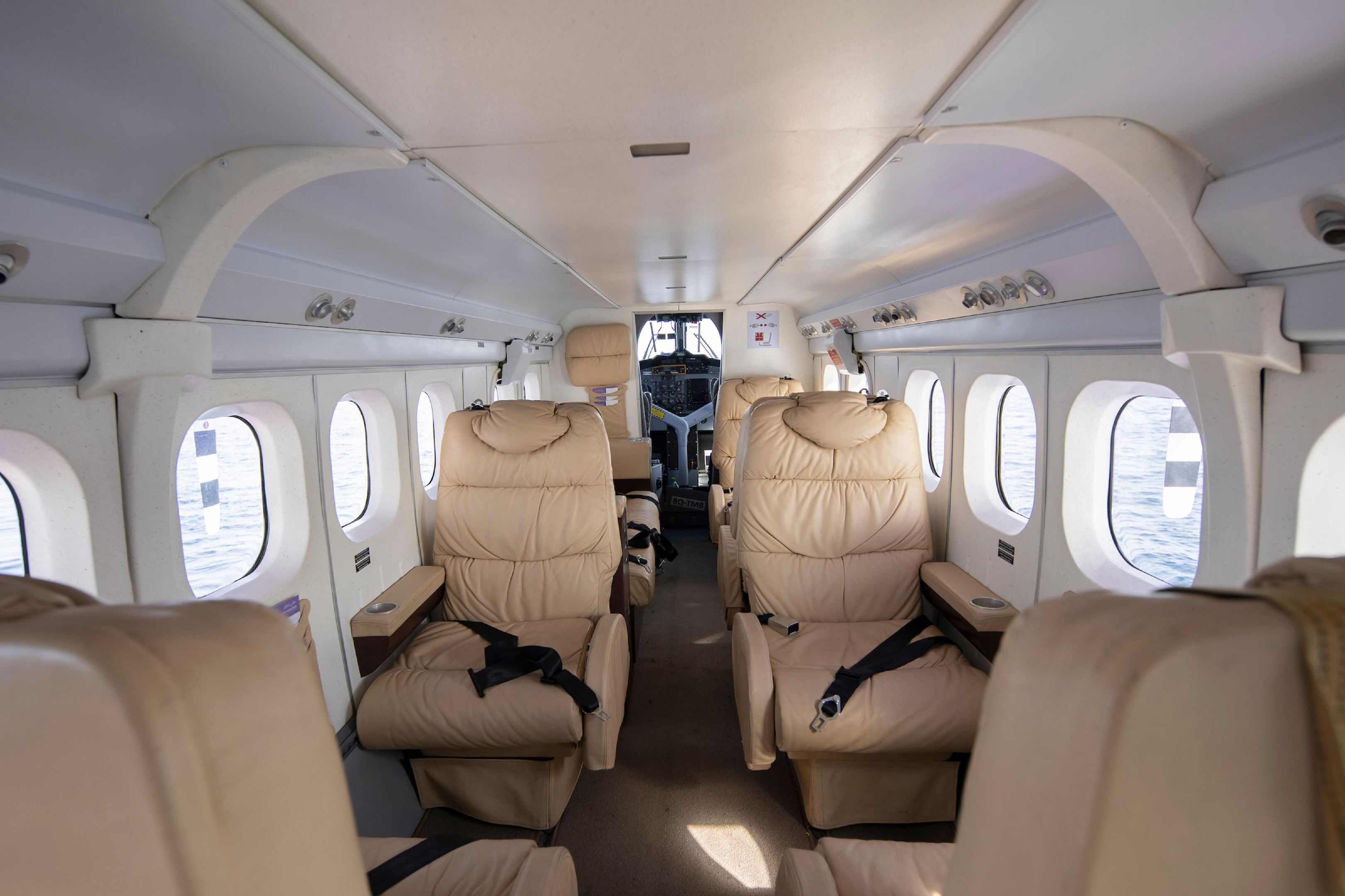 The interior of an airplane cabin with rows of beige leather seats and windows.