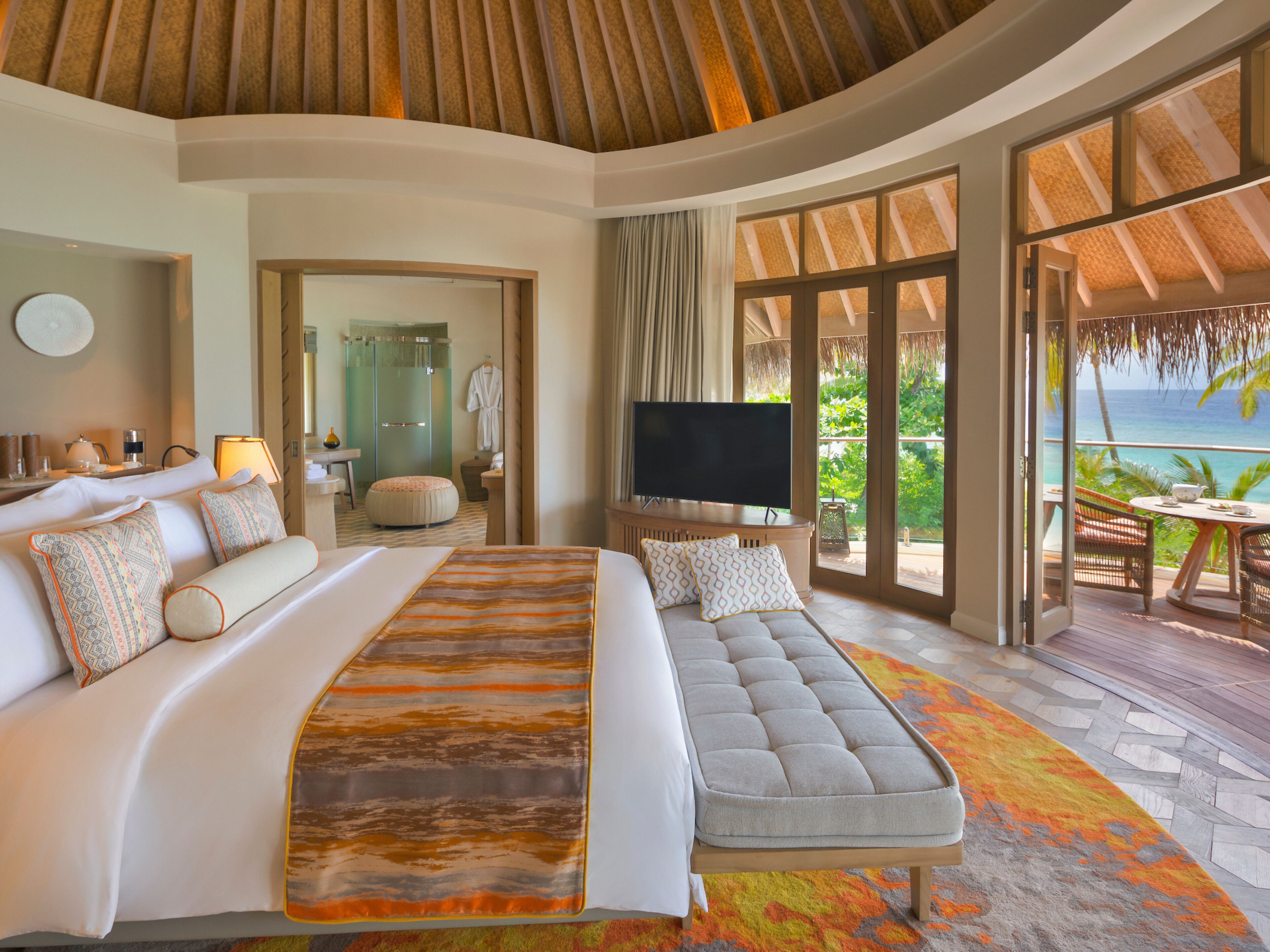 A spacious bedroom with a large bed, a sofa, a TV, and a balcony with a view of the ocean.