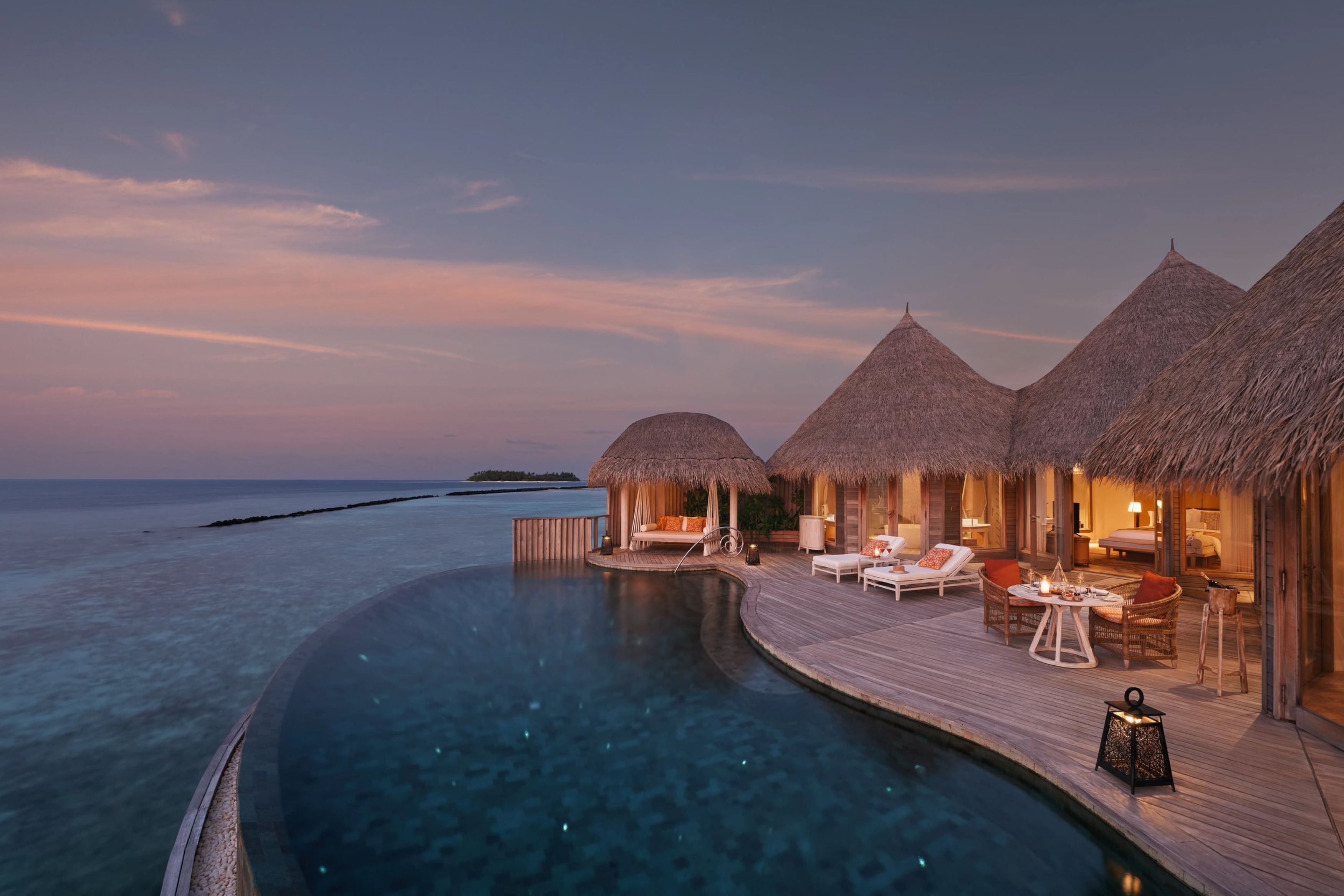 An overwater villa with a private infinity pool, thatched-roof structures, and a wooden deck with outdoor seating.