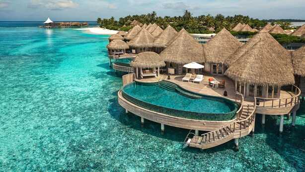 Bungalows sobre el agua con techos de paja, pasarelas de madera y sillones de descanso.