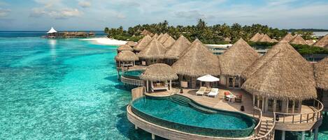 An overwater villa with thatched-roof structures, infinity pools, and a clear view of the turquoise sea.