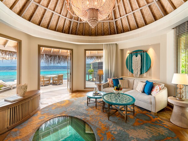 A spacious living area with a view of the ocean, a round table, a sofa with colorful cushions, and a unique ceiling design. - The Nautilus Maldives (Thiladhoo)