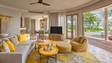 A spacious living room with a large TV, yellow and white furniture, and a view of the ocean.