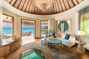 Amplia sala de estar con un gran ventanal con vistas al mar, una mesa de centro redonda, un sofá con cojines de colores y un tapiz decorativo.