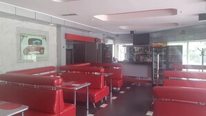 A retro diner with red booths and chrome tables, a vintage car poster on the wall, and a bar area with a jukebox. - Sapsan (Pavlodar)