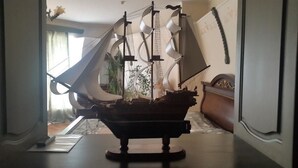 A model ship on a table in a room with a window, a plant, and a wooden cabinet. - Sapsan (Pavlodar)