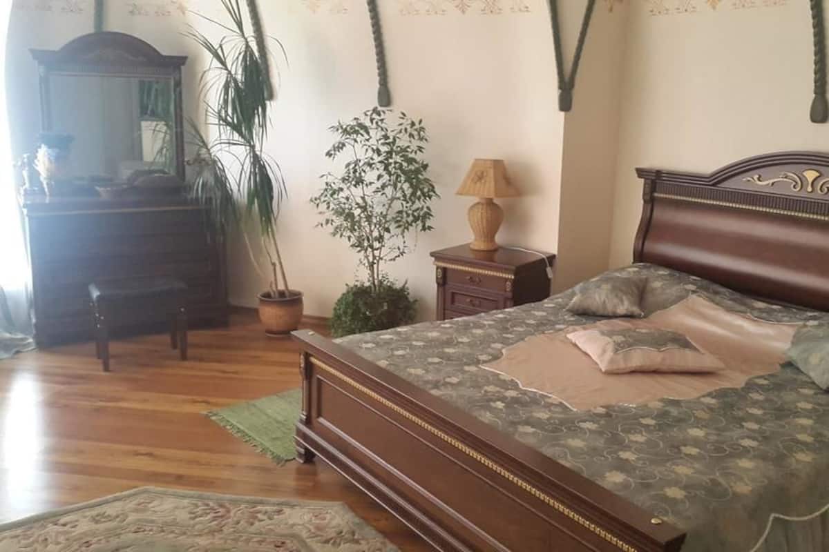 A bedroom with a wooden bed, a dresser, a lamp, and two potted plants.