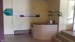 A reception area with a curved reception desk, a potted plant, and a directional sign on the wall. - Sapsan (Pavlodar)
