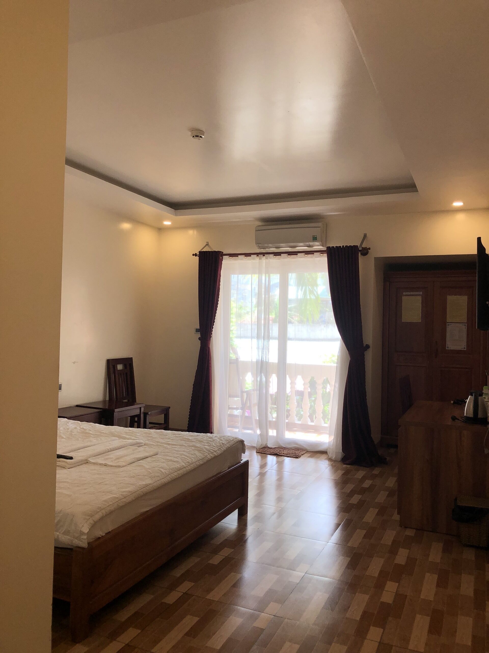 Une chambre avec un lit en bois, un bureau, une chaise et une armoire. Une porte-fenêtre coulissante donne accès à un espace extérieur.