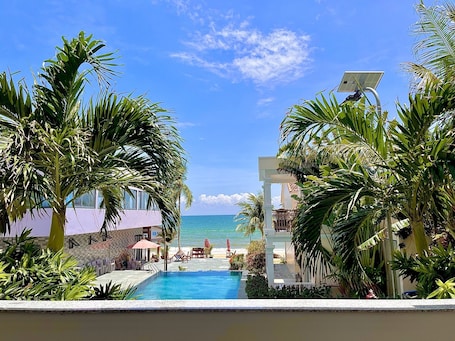 A pool area with a view of the ocean, surrounded by palm trees and a building with a white facade.