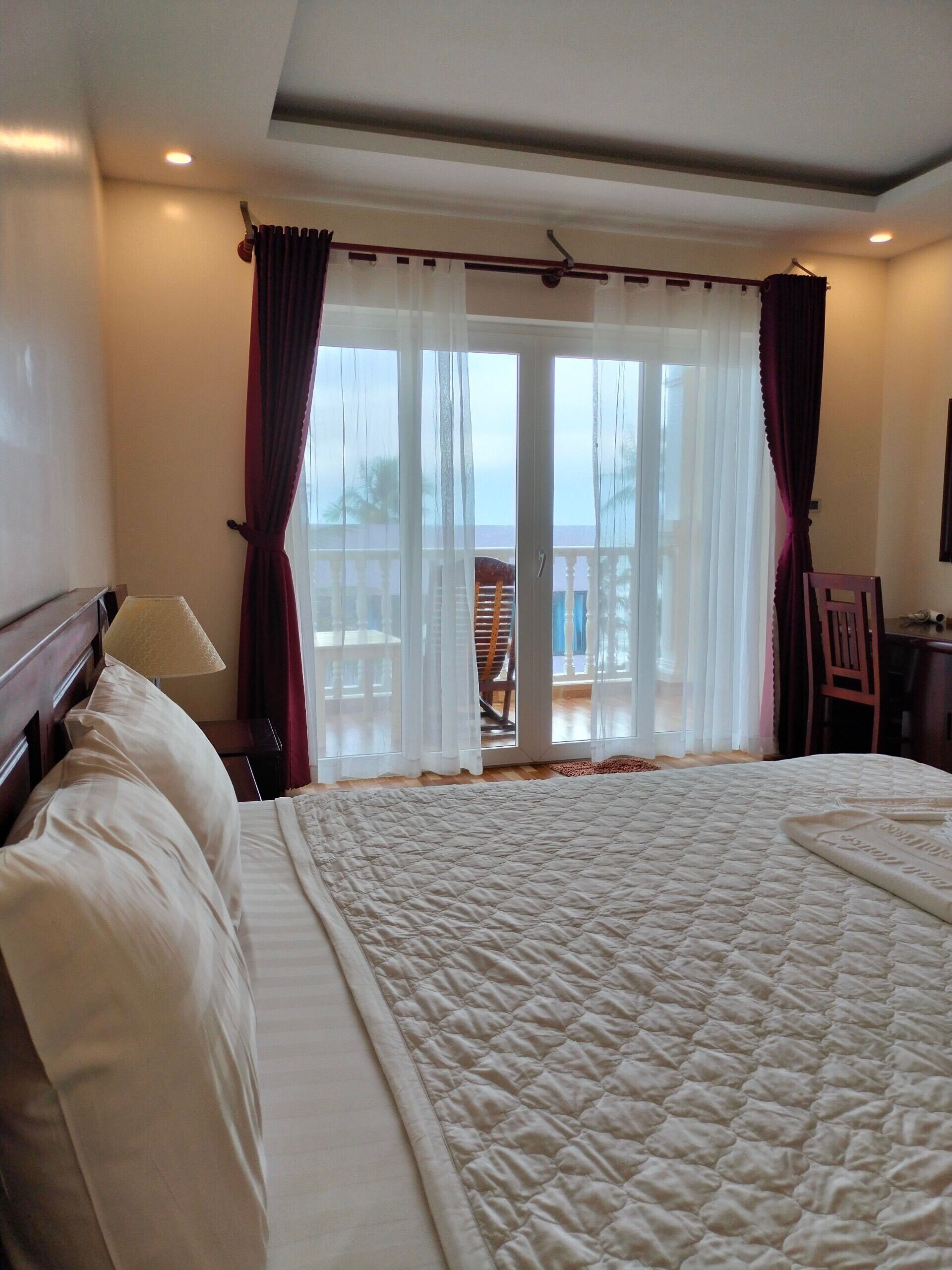 A hotel room with a large bed, a desk, a chair, and a balcony with a view.