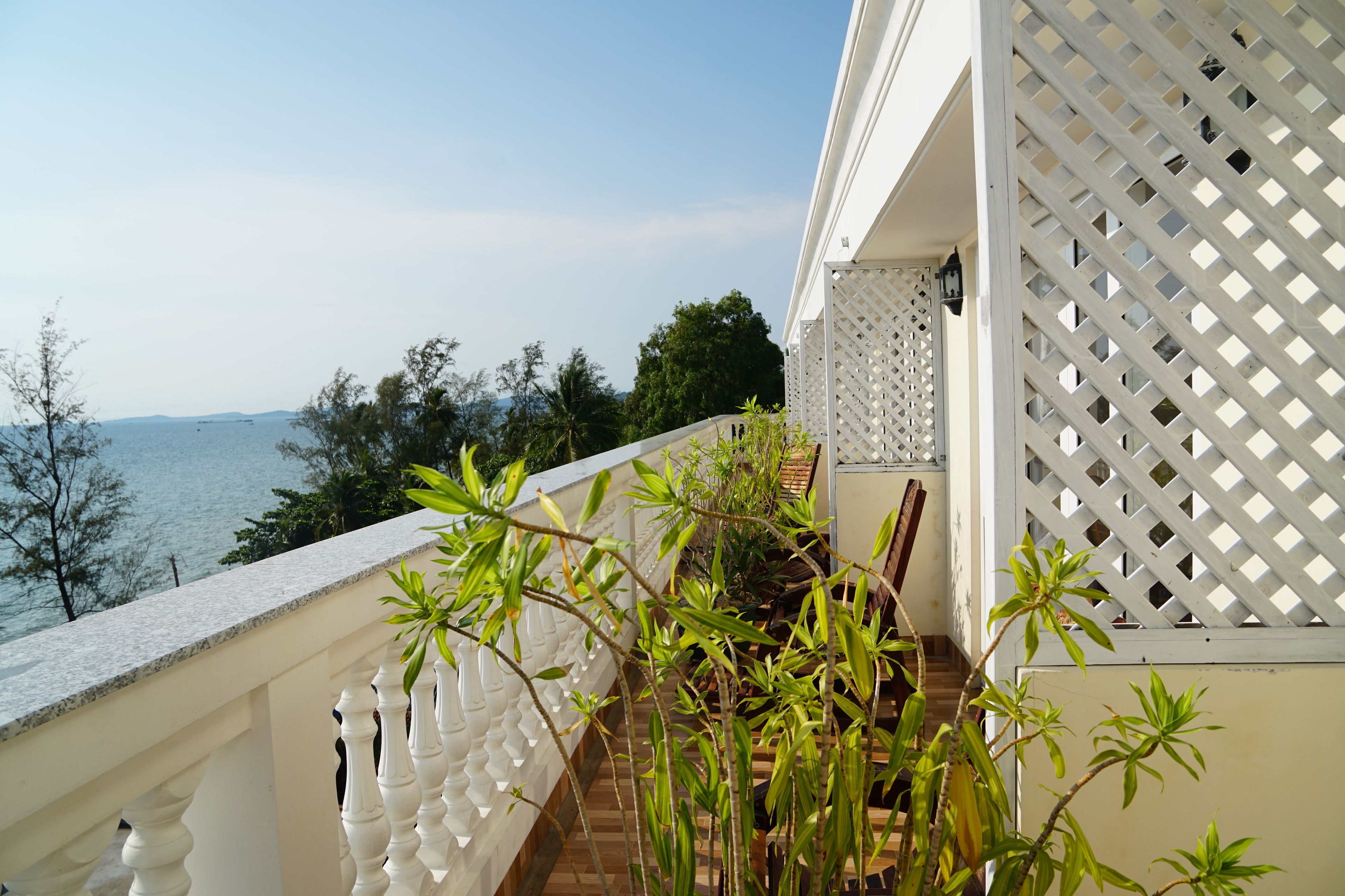 A balcony with a view of the sea, white balustrades, and potted plants.