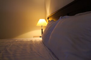 Una cama bien hecha con sábanas blancas y una lámpara de noche que ofrece una iluminación suave.