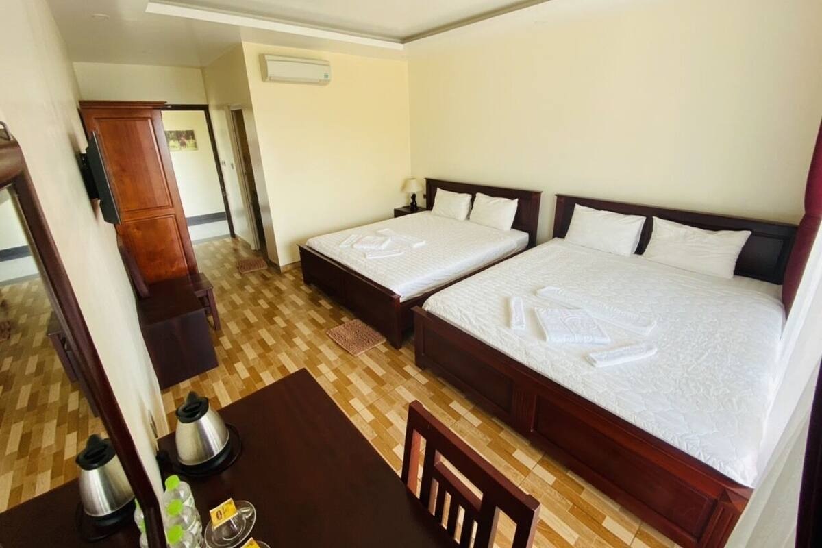 Una habitación de hotel con dos camas, un armario de madera, un escritorio con una silla y una cafetera.