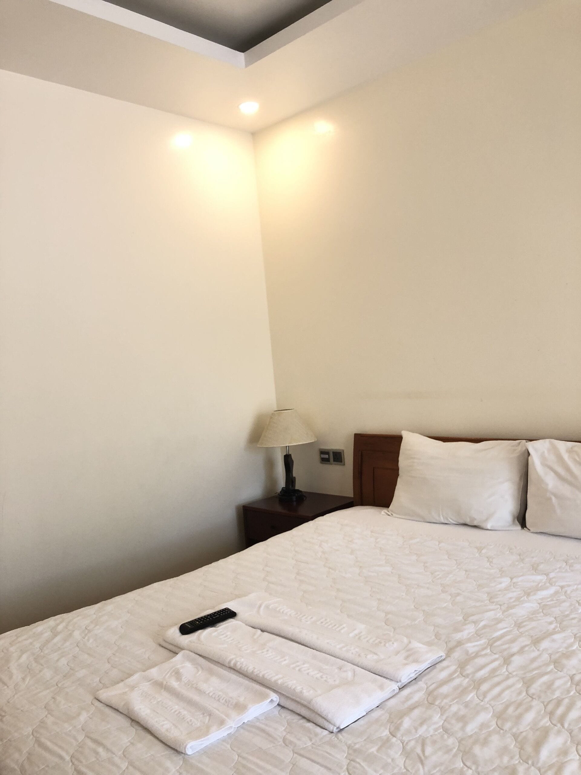 A hotel room with a large bed, a nightstand with a lamp, and a remote control on the bed.