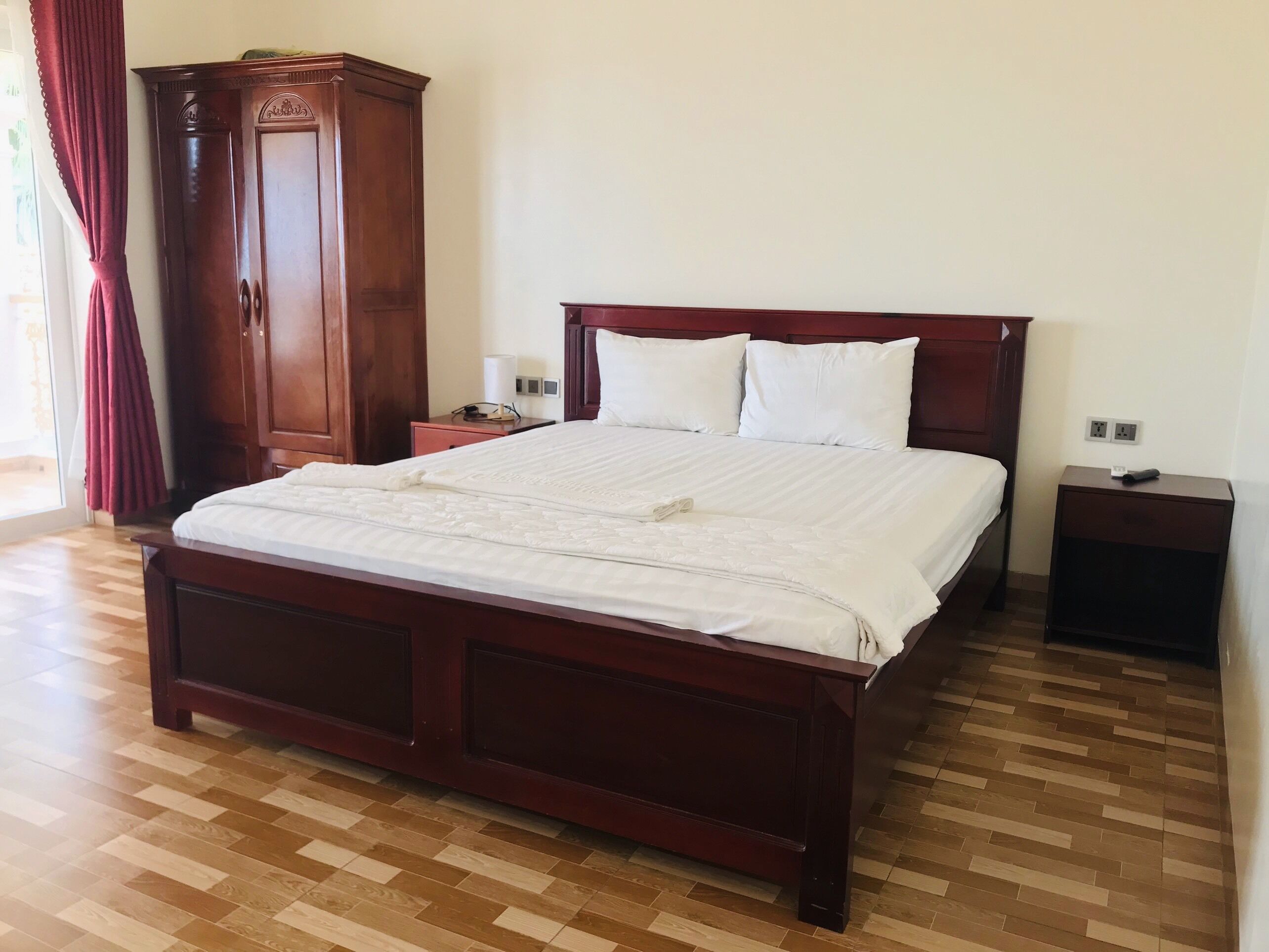 A neatly made bed with a wooden headboard, a wooden wardrobe, and a nightstand with a lamp.