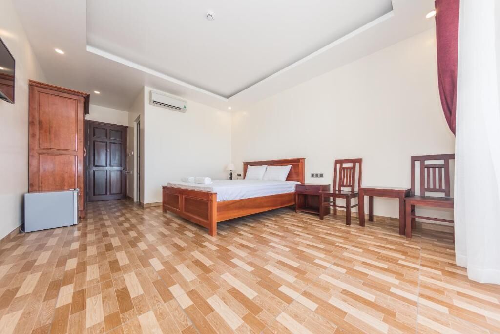 A bedroom with a wooden bed, a desk, and a chair. There is a radiator and an air conditioning unit on the wall.