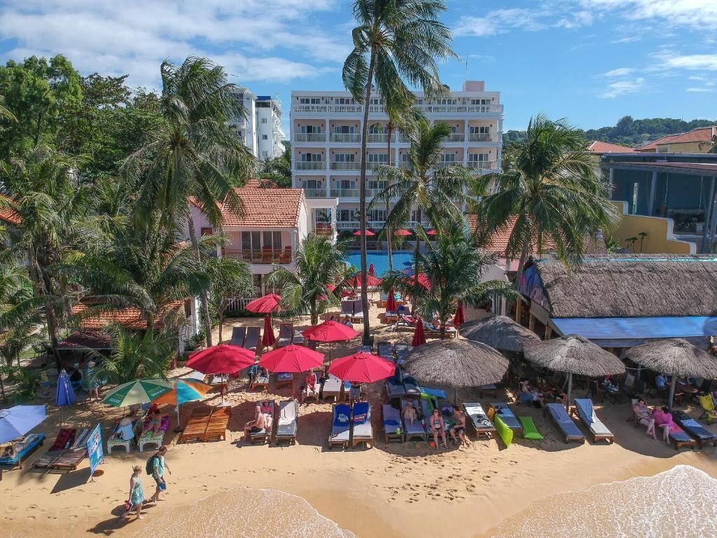 Un complejo turístico en la playa con numerosas tumbonas, sombrillas y palmeras.