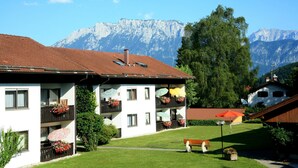 Ein zweistöckiges Gebäude mit Balkonen, einem Rasen und einem Berg im Hintergrund.