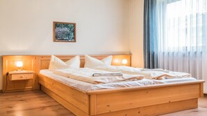 Ein hölzernes Bett mit Kopfteil, zwei Nachttische mit Lampen, ein kleines gerahmtes Bild an der Wand und ein Fenster mit Vorhängen.