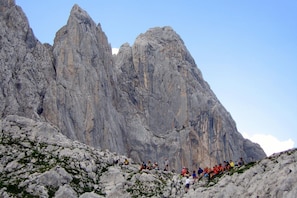 Een groep wandelaars op een rotsachtig bergpad, met steile kliffen op de achtergrond.