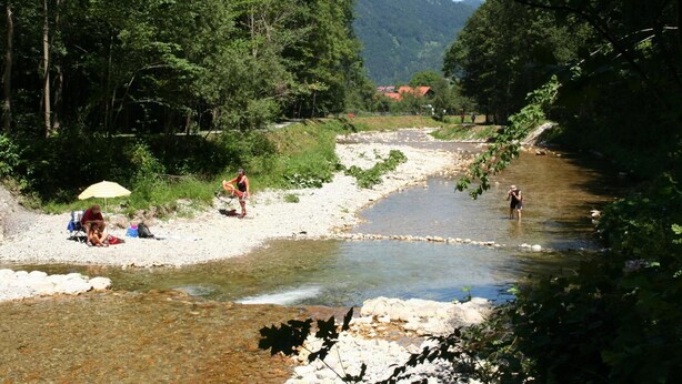 Ein Flussufer mit entspannten Menschen und einem Berg im Hintergrund.