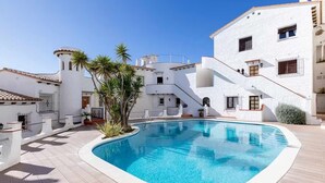 A swimming pool surrounded by white buildings with balconies and palm trees.