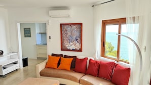 A modern living room with a curved sofa, a coffee table, and a large window offering a view of the sea.