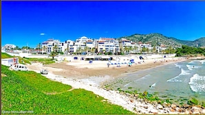 A coastal hotel with multiple buildings, a beach, and a mountainous backdrop.
