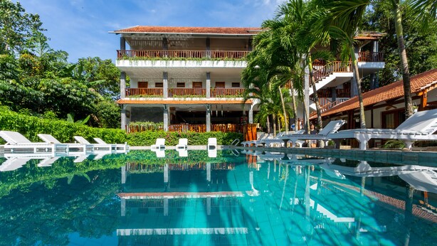 Un hotel con piscina, varios balcones y abundante vegetación.